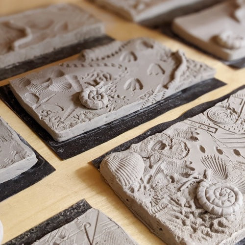 Clay tiles pressed with fossil and shell shapes, drying on a board
