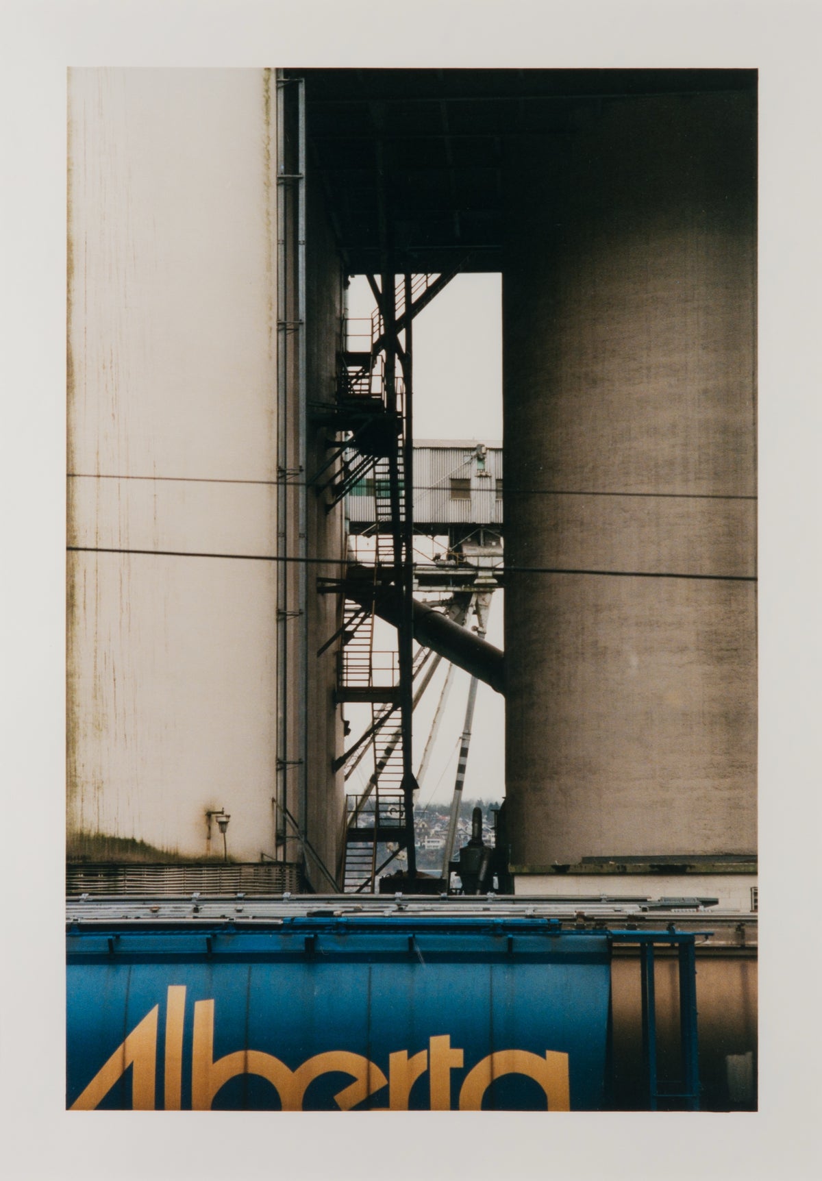 Wayne Eastcott, Moodyville Notes #3, 2002. Photograph of overlapping architecture with a billboard with the word "Alberta" on the bottom.