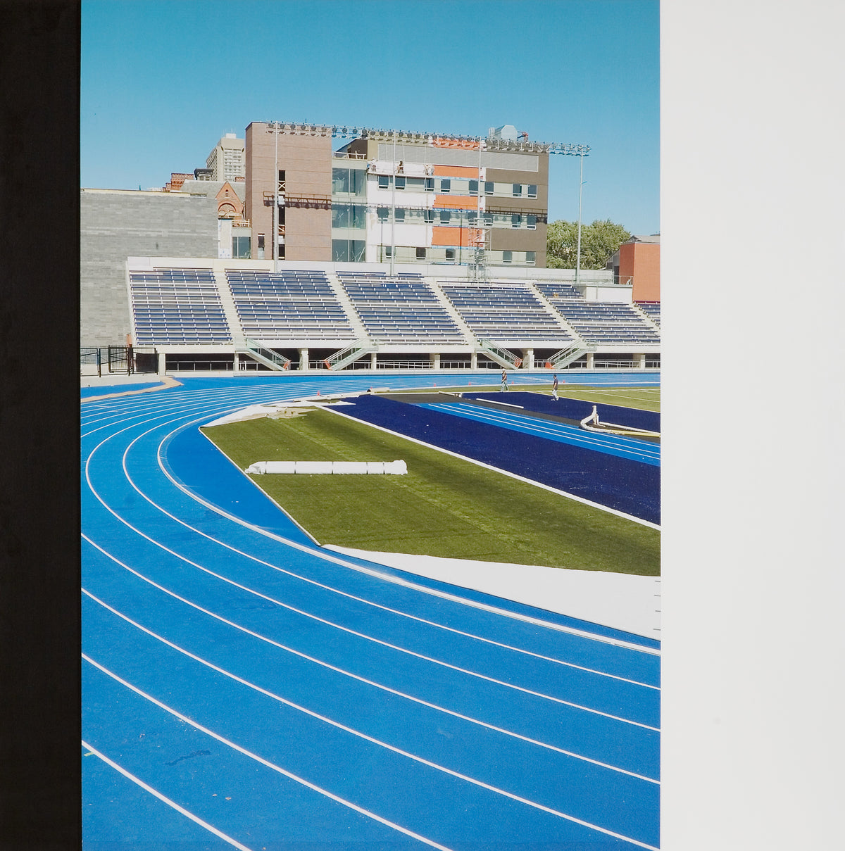 Ian Wallace, Blue Field, 2007. Image of a blue track with bleachers against buildings in the background on clear blue sky.