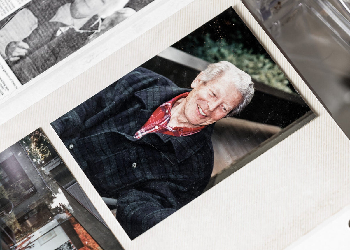 An album page holding a colour photograph of smiling artist Gordon Smith with distinctive white hair in a plaid jacket and red shirt