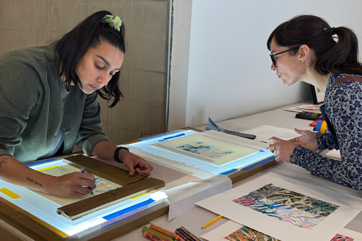 Russna Kaur and Jillian Ross working on the edition at a light table with various art supplies.