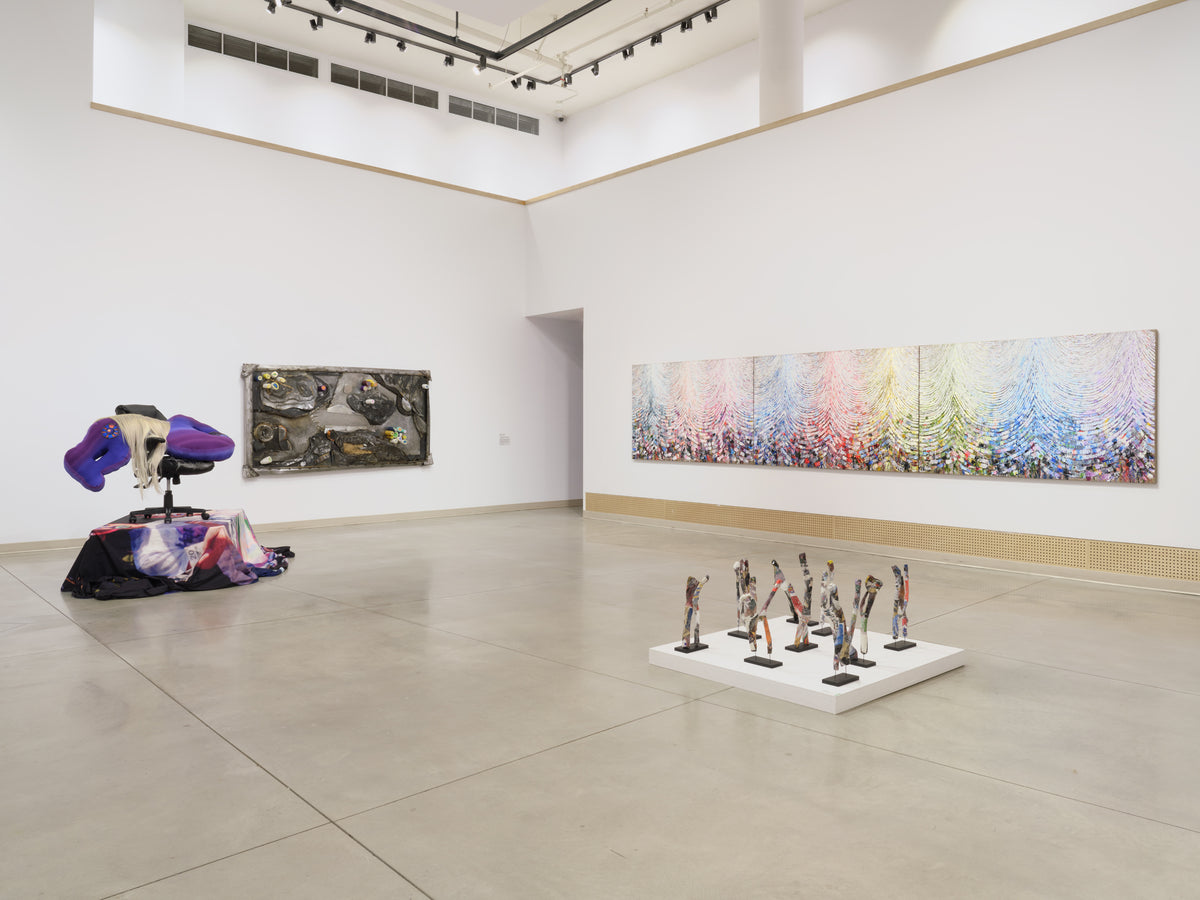 A long rainbow-coloured triptych painting, a dark wall relief, a draped office chair sculpture and small standing figures on a low plinth