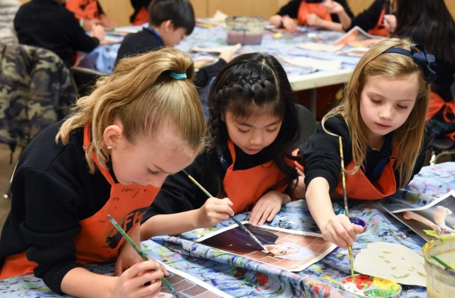 Three students in orange aprons painting at a table in an After School Art class