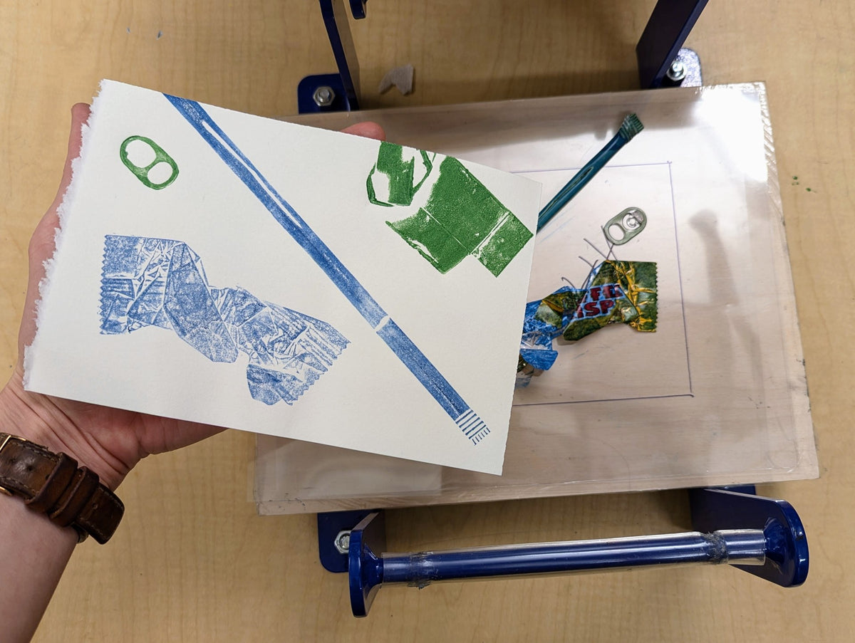 A collagraph print in blue and green lifted from its printing plate on a small press