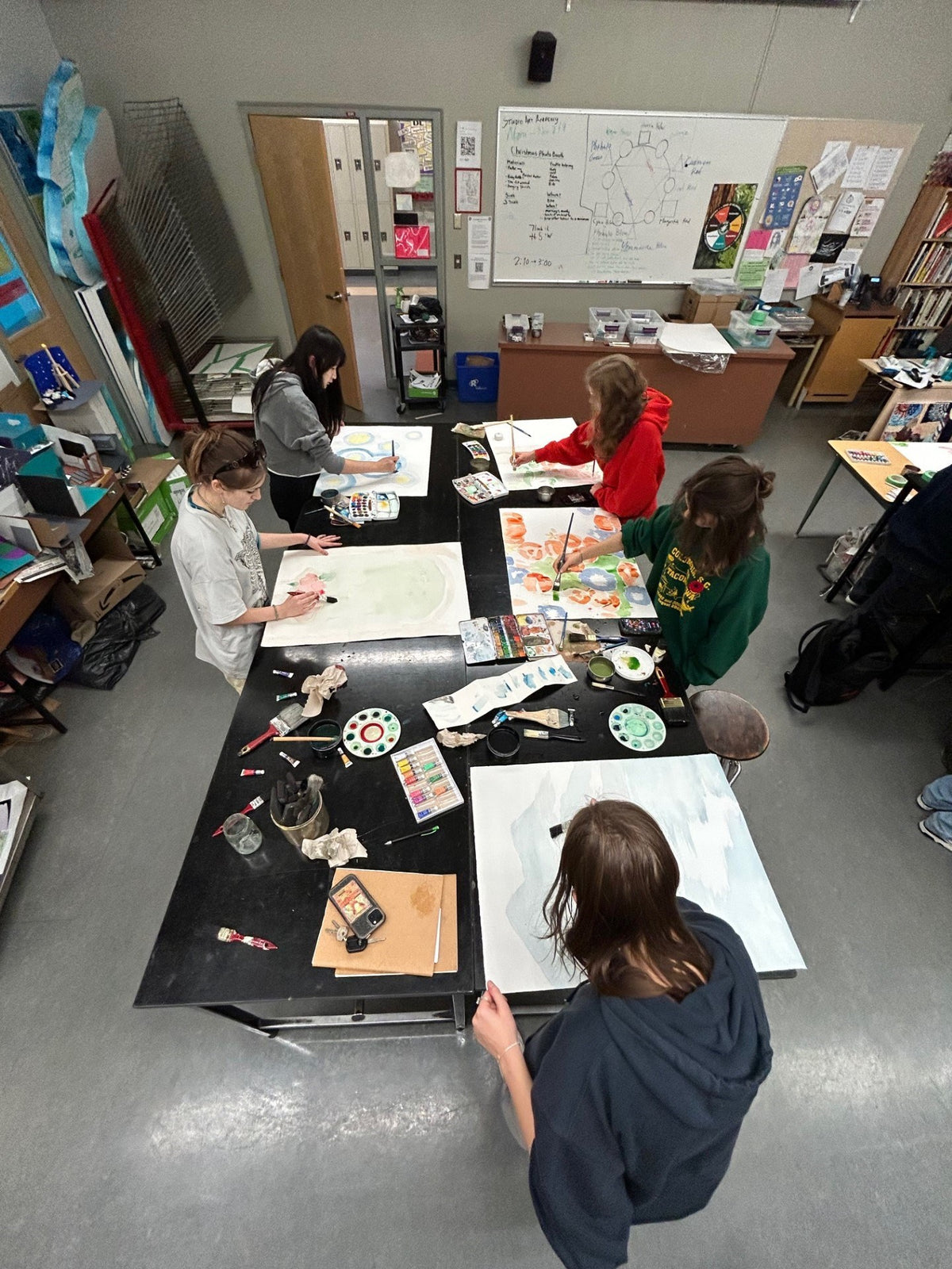 Students painting at tables in a classroom studio, seen from above