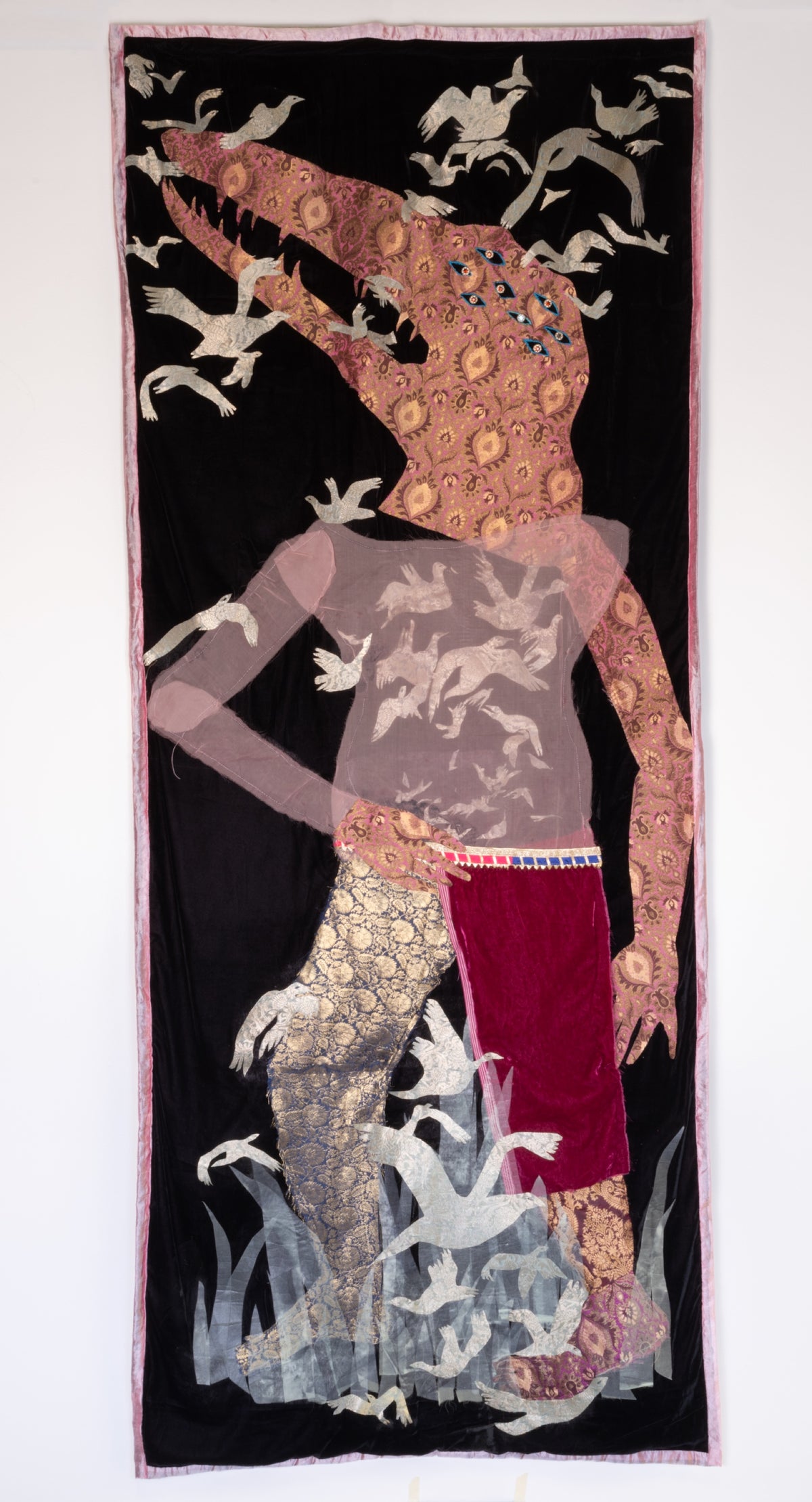 Sara Khan, Renegade Mothers: Crocodile Breath, 2023. An alligator-like humanoid creature, adorned in decorative outfit, standing in a small patch of grass and surrounded by birds.