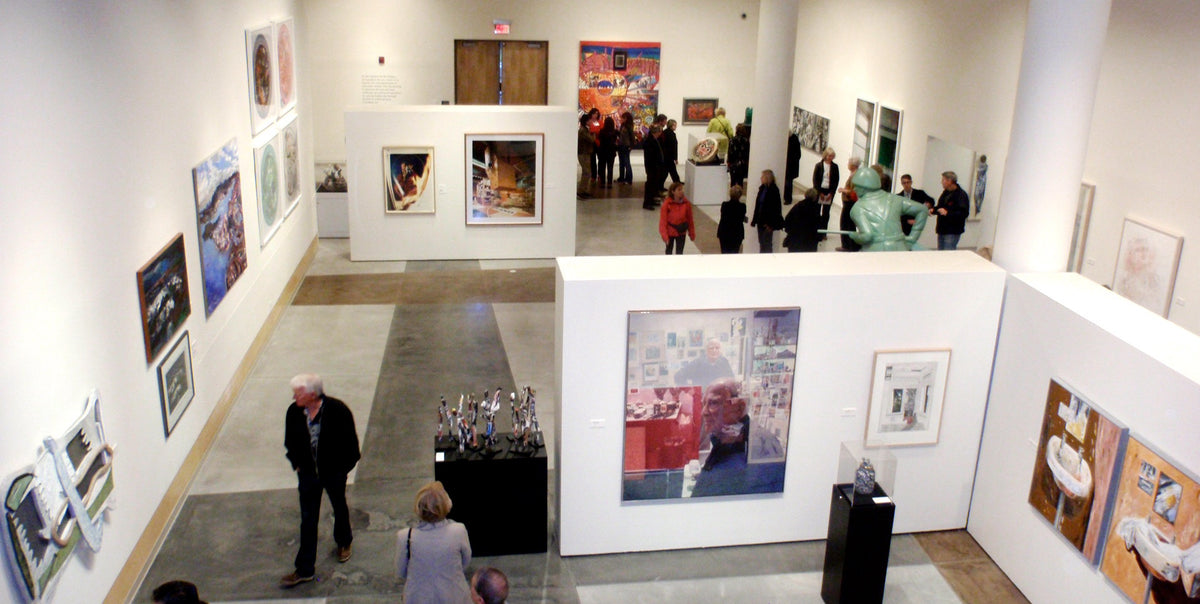 Seen from above, visitors walk through a white gallery hung with paintings, prints and photographs, with sculptures on black plinths