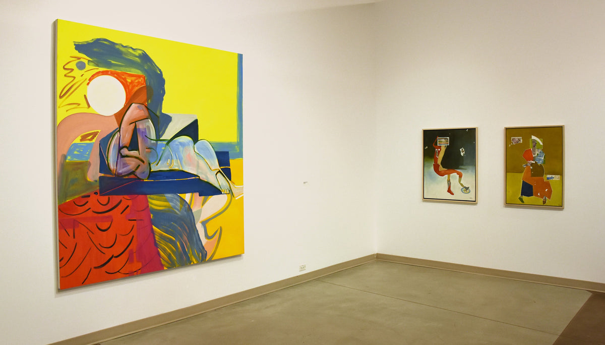 A large yellow, red and blue painting of a reclining figure hangs beside two smaller framed paintings of standing figures